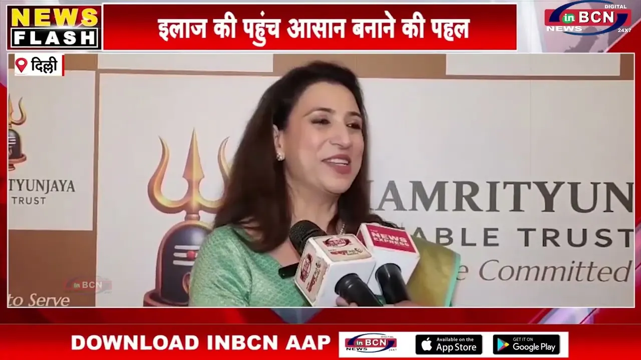 Ritu Kalia speaking to a cluster of reporters' microphones in front of the Trust's banner, in the INBCN News report